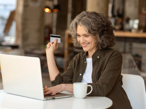 Mulher segurando cartão em frente ao notebook